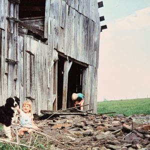 two blond children and border collie playing in front of abandoned barn