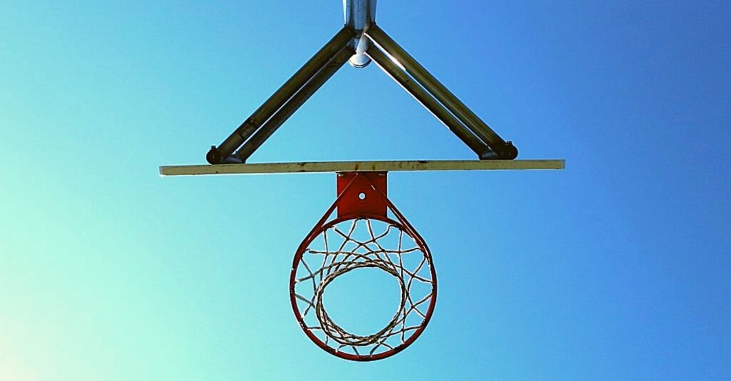 image of basketball hoop from below, silhouetted against a blue sky